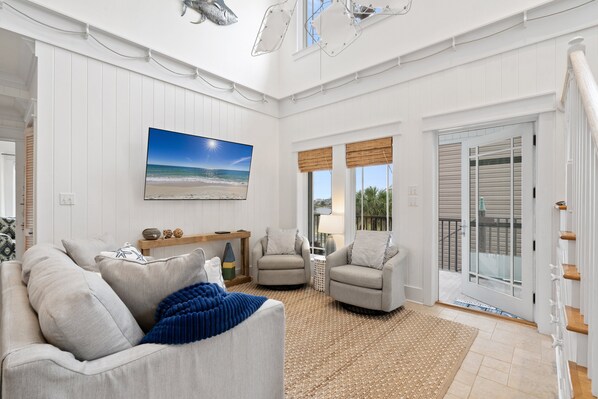 A spacious living room with a large flat-screen TV, two armchairs, a sofa, and a coffee table.