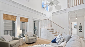 Un salon spacieux avec un plafond haut, un escalier et une grande fenêtre dotée de volets.