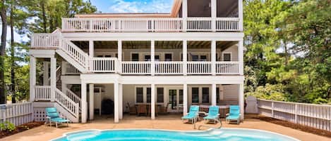 A two-story house with a pool, outdoor furniture, and a wooden deck.