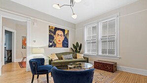A living room with a sofa, two chairs, a glass coffee table, a painting, and a window with blinds. - Stunning Townhouse in an Amazing Location Near Fiserv, Baird Center, Lakefront (Milwaukee)