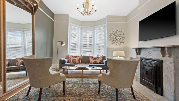 A living room with a fireplace, a television mounted on the wall, and a large window with blinds. - Stunning Townhouse in an Amazing Location Near Fiserv, Baird Center, Lakefront (Milwaukee)