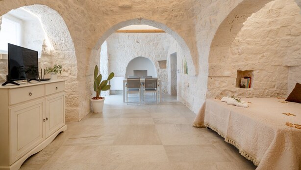 A room with a stone wall, a bed, a desk with a computer, and a dining area with chairs and a table. - GuestHost - Trulli Miriam: Enchanting Apulian Getaway (Martina Franca)