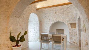 A stone-walled room with a dining table and chairs, a potted plant, and an arched ceiling. - GuestHost - Trulli Miriam: Enchanting Apulian Getaway (Martina Franca)