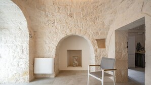 A room with a stone wall, a white radiator, a chair, and a small shelf with a vase. - GuestHost - Trulli Miriam: Enchanting Apulian Getaway (Martina Franca)