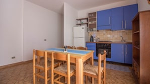 Una cocina compacta con armarios azules, una mesa de comedor con sillas y un refrigerador.
