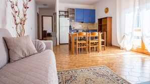 Una sala de estar con un sofá, una mesa de comedor con sillas, una zona de cocina con armarios azules y una alfombra estampada.