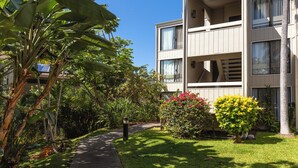 A two-story building with a balcony on the upper floor, surrounded by lush greenery and a well-maintained lawn.
