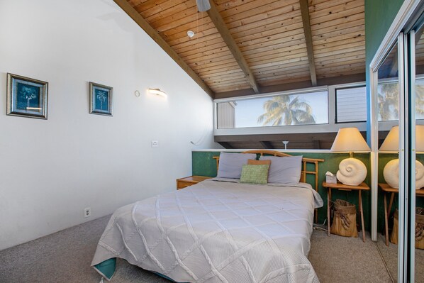 A bedroom with a bed, wooden headboard, two bedside tables with lamps, and framed pictures on the wall. - 🌴Centrally Located | AC | Ocean View | Kailua Bay Resort 4-305🌴 (Kailua Kona)
