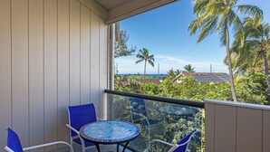 A balcony with a table and chairs, overlooking a residential area with palm trees and a view of the ocean.