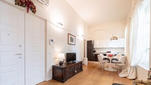 Una sala de estar con televisor, un mueble de madera, un comedor con sillas y una cocina al fondo.