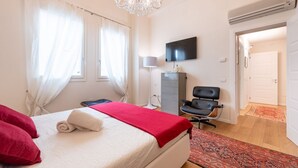 Un dormitorio con cama, televisión, escritorio, silla y candelabro.