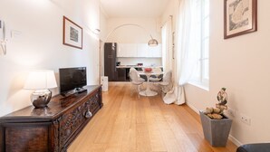 Una cocina moderna con armarios blancos, un comedor con mesa y sillas redondas, piso de madera y una pequeña planta decorativa.