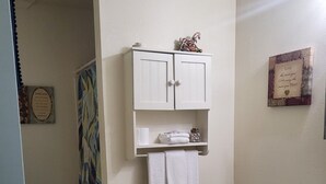 A bathroom with a toilet, a sink, a towel rack with towels, a cabinet with decorative items, and a shower curtain.