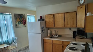 A compact kitchen with wooden cabinets, a white refrigerator, a microwave, a sink, and a stove.