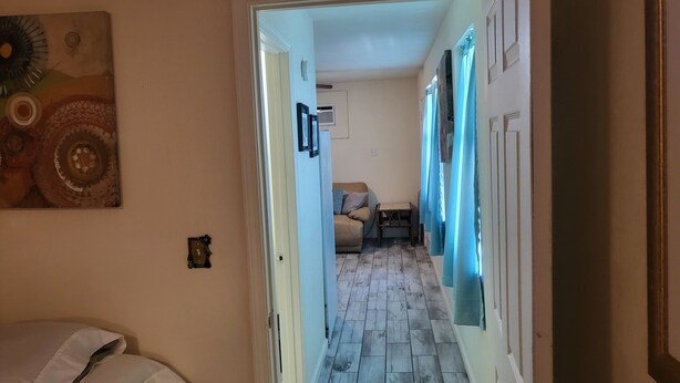 A hallway with a bed, a small table, and a door leading to another room.