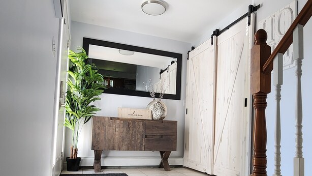 Ein Flur mit einer Holzbank, einem Willkommensschild, einem Blumentopf und einem Spiegel an der Wand.