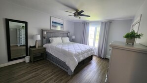 Ein Schlafzimmer mit Bett, Nachttischen, Deckenventilator, Kommode und einem Fenster mit Vorhängen.