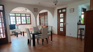 Amplia sala de estar con una mesa de comedor de vidrio, sillas blancas, un sofá y un televisor.