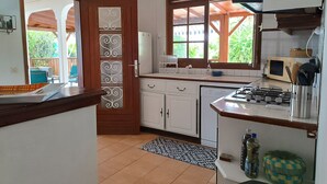 Una cocina con gabinetes blancos, una estufa, un microondas y un fregadero. Hay un tapete estampado en el suelo y una ventana con vistas a la vegetación.