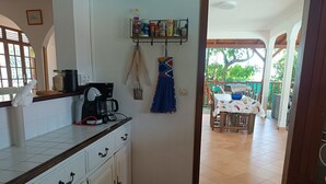 Una cocina con una cafetera, frascos y una toalla colgando. Hay un comedor con mesa y sillas afuera.