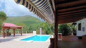 Una piscina con terraza de madera y zona cubierta con toldo a rayas.