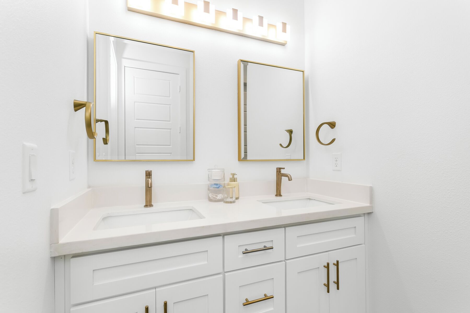 A modern bathroom with two sinks, gold fixtures, and a vanity with drawers.