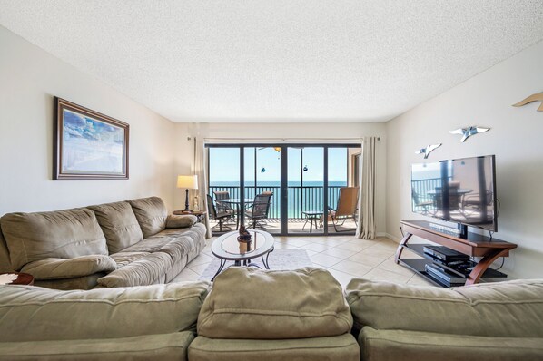 A living room with a sofa, a coffee table, a TV, and a balcony with a view of the sea.