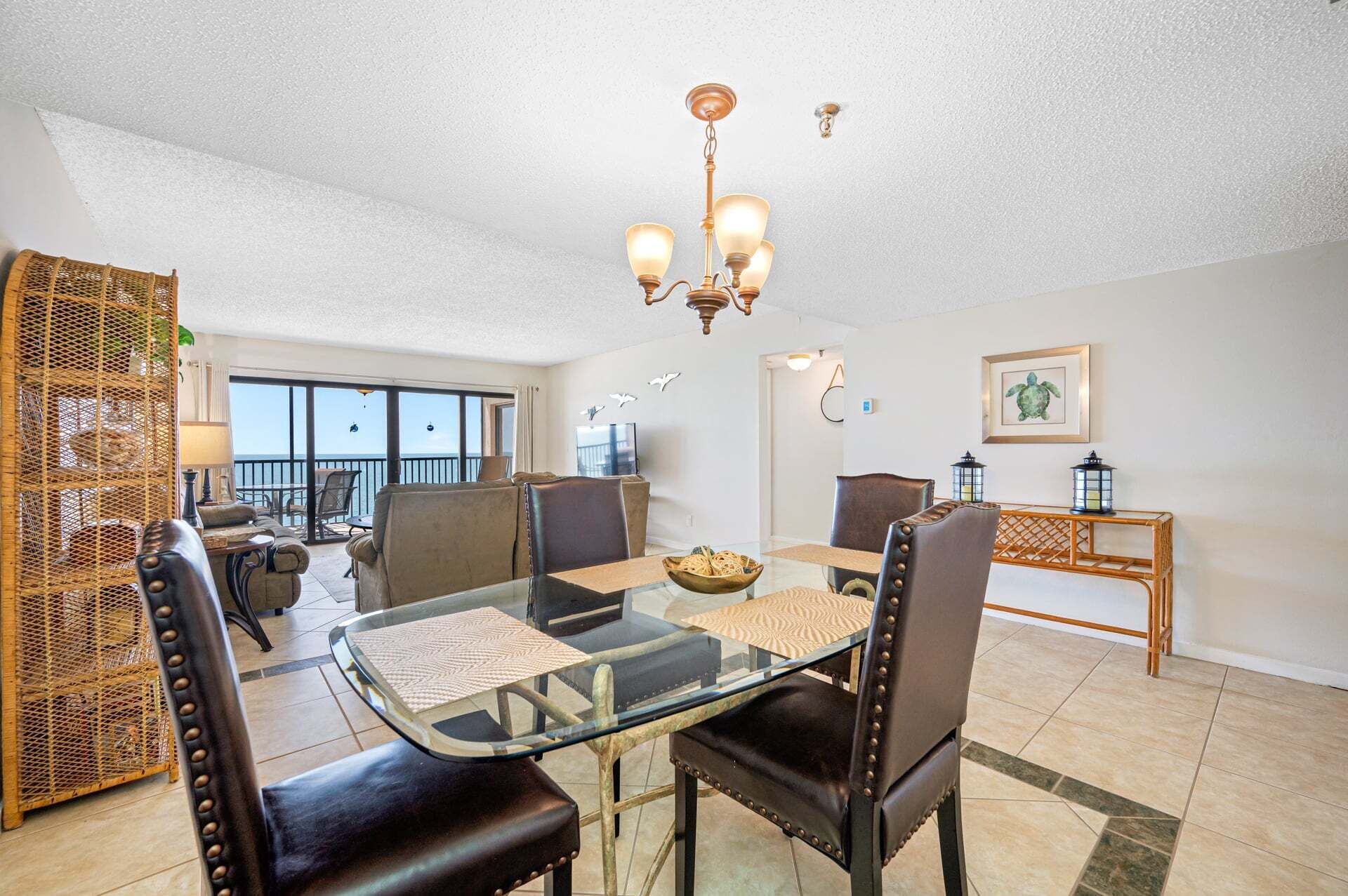A dining area with a glass table, leather chairs, a chandelier, and a view to the outside.