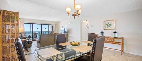 A dining area with a glass table, leather chairs, a chandelier, and a view to the outside.