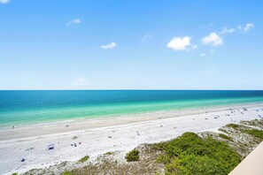 A beach with clear turquoise water, sandy shore, and sparse vegetation.