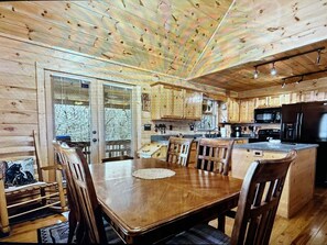 A wooden cabin interior with a dining table, chairs, a kitchen area with appliances, and a view through the glass door. - Peaceful Blue Ridge Mtn Cabin-Gated, WiFi, Hot Tub, Fire Pit, Game Room (Blue Ridge)