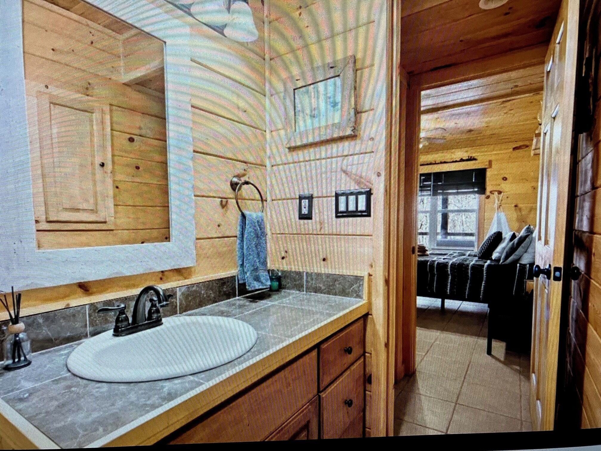 Une salle de bain rustique, avec des murs en bois, comprenant un grand miroir, un lavabo et un porte-serviettes.