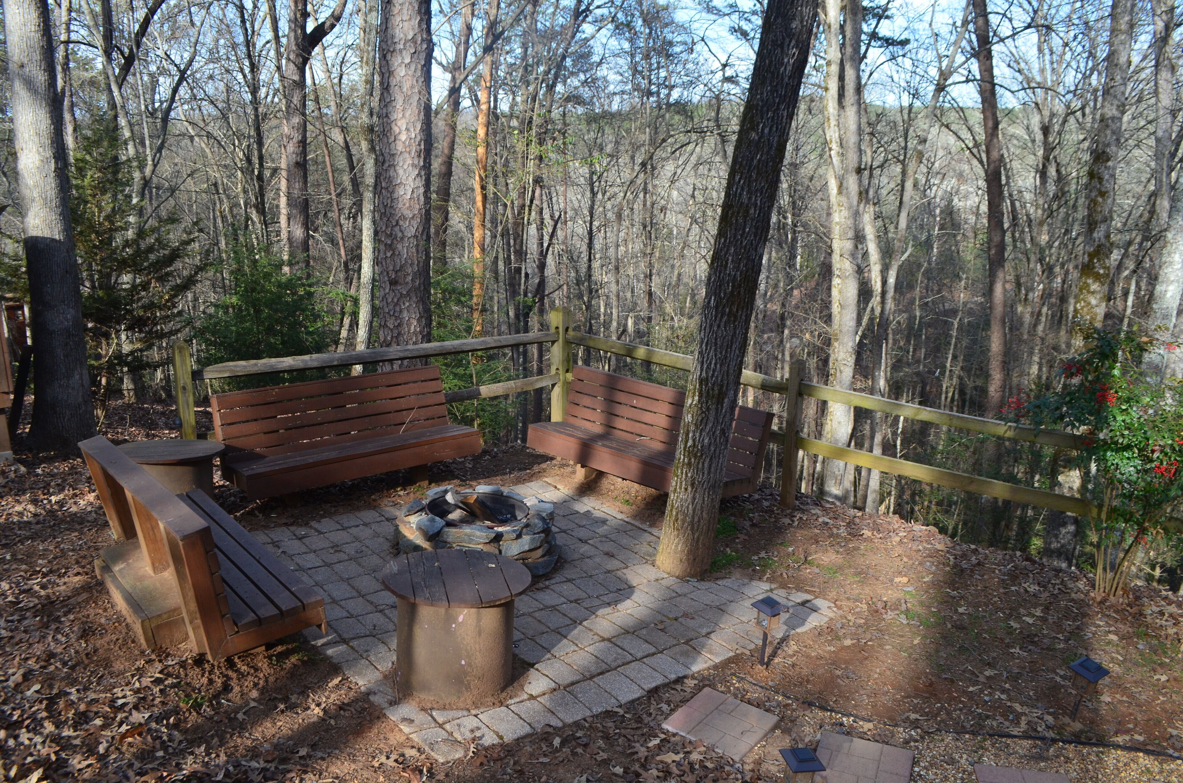 Un banc en bois et un foyer, situés dans une zone boisée et entourés d’une clôture en bois.