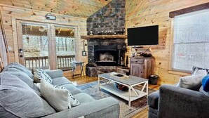 A cozy log cabin interior with a fireplace, a television mounted on the wall, and a seating area with sofas and a coffee table. - Peaceful Blue Ridge Mtn Cabin-Gated, WiFi, Hot Tub, Fire Pit, Game Room (Blue Ridge)