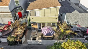 Une maison à deux étages dotée d’un patio, d’un espace extérieur couvert aménagé en salon et de diverses plantes en pot.