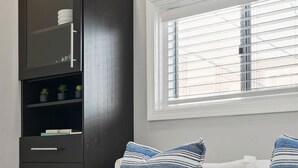 Une chambre à coucher avec un lit, deux oreillers, une armoire en bois foncé et une fenêtre avec des stores.