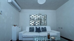 A modern living room with a white sofa, a glass coffee table, and a decorative mirror on the wall.