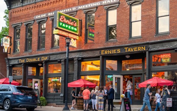 A brick building with a neon sign for 'Ernie's Tavern' and 'The Double Dip' across the street.