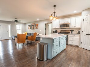 A spacious kitchen with white cabinets, a central island, and a dining area with orange chairs.