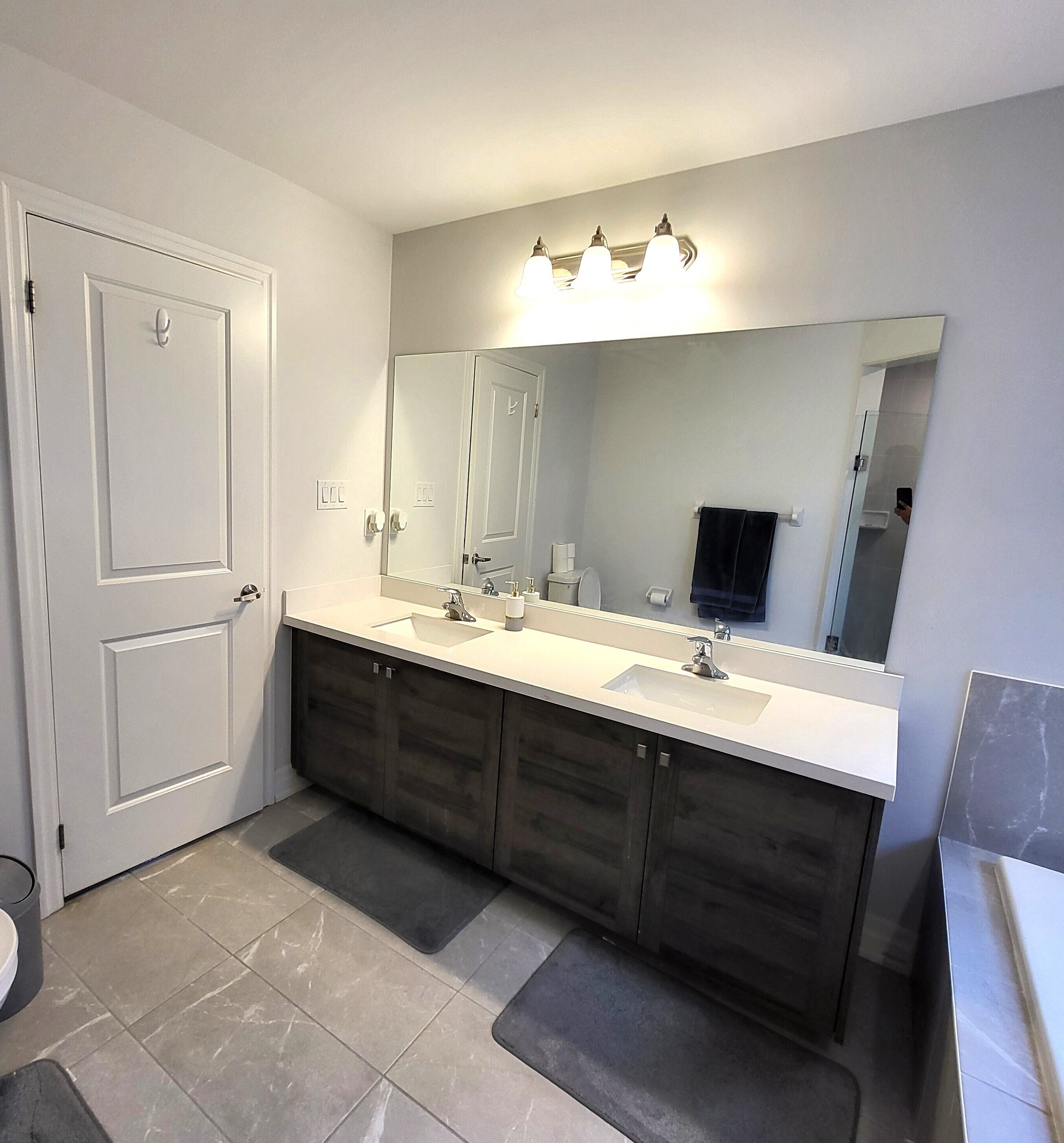A bathroom with a double sink vanity, a large mirror, and a door.