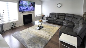A modern living room with a sectional sofa, a flat-screen TV mounted on the wall, a fireplace, and a large window providing natural light. - Spacious 4 Bedroom House in Angus (Angus)