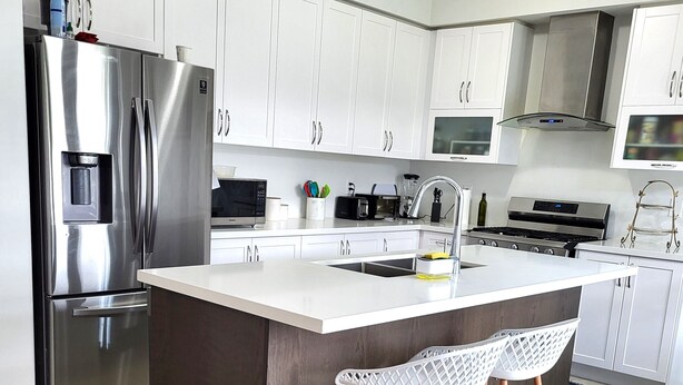 A modern kitchen with stainless steel appliances, white cabinetry, and a central island with bar stools. - Spacious 4 Bedroom House in Angus (Angus)