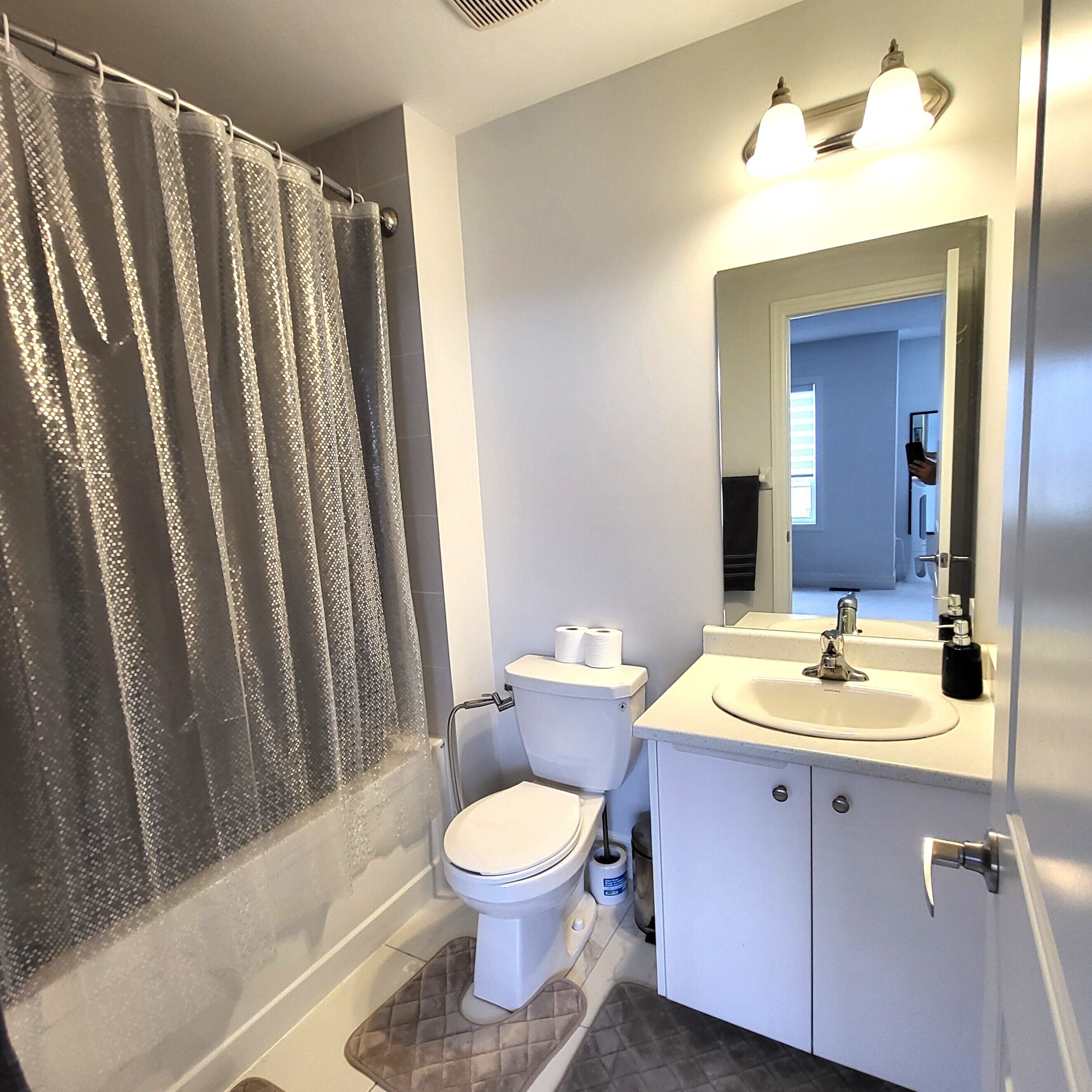 A bathroom with a shower curtain, toilet, sink, and mirror.
