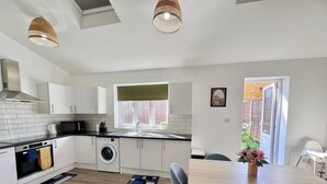 Une cuisine moderne avec des meubles blancs, un four encastré, un lave-linge et un coin repas comprenant une table et des chaises.