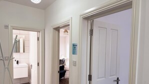 Un couloir avec des portes blanches, une salle de bain blanche avec un miroir et un panneau d’accueil.