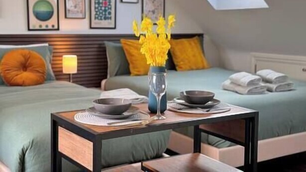 A bedroom with two beds, a skylight, and a table with a vase of yellow flowers.