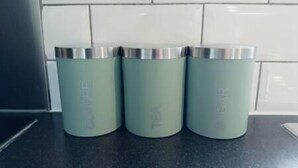 Three teal-colored containers with silver lids on a kitchen counter.