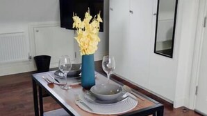 A dining table with a vase of yellow flowers, two wine glasses, and a set of plates and cutlery.