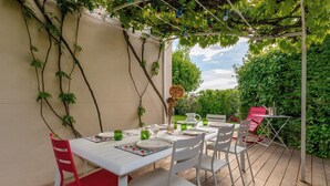 An outdoor patio with a white table set for dining, surrounded by white chairs, and a red chair. - Villa Juliette - Welkeys (Écully)