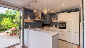 A modern kitchen with white cabinetry, a central island, pendant lighting, and a view of the garden through a glass door. - Villa Juliette - Welkeys (Écully)